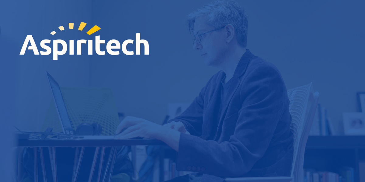 A man with short gray hair and glasses working on a laptop at a desk, with the Aspiritech logo in the top left corner over a blue graphic overlay.